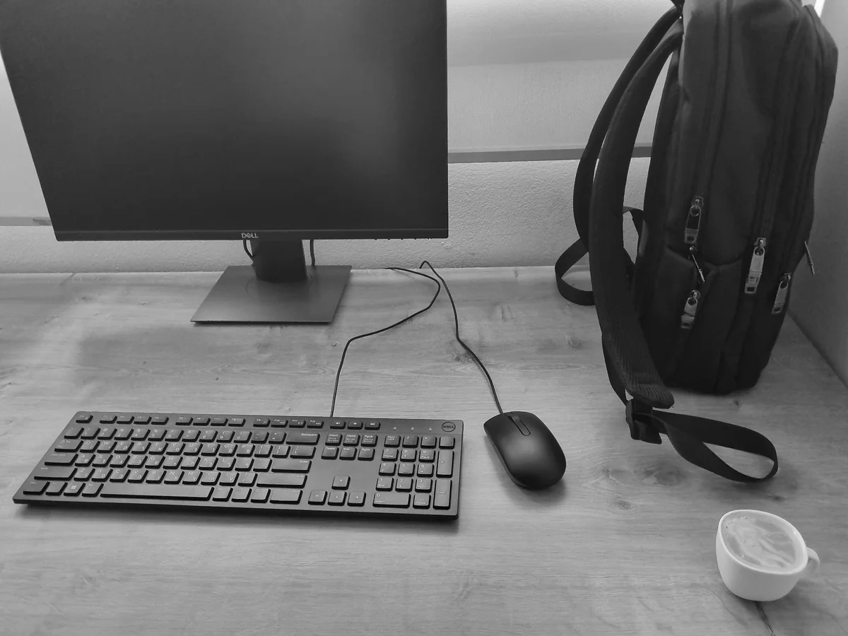 Black-and-white desk with monitor, keyboard, mouse, backpack, and coffee