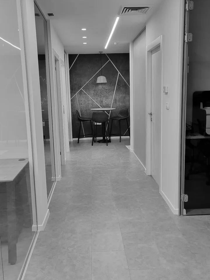 Black-and-white office hallway with glass rooms and a small meeting area